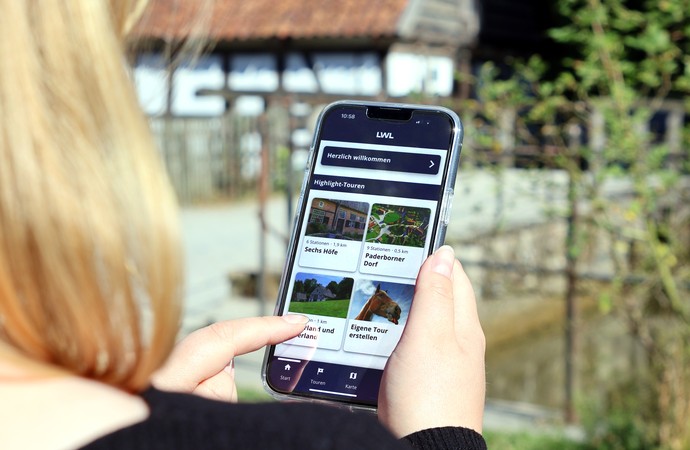 Eine Frau blickt auf ihr Handy, im Hintergrund die Wassermühle