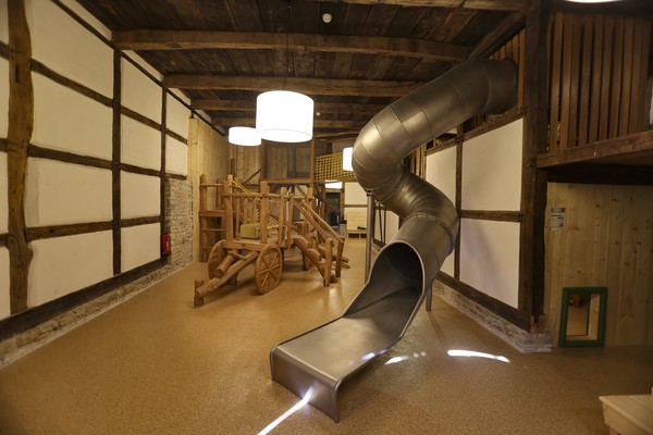 Spielplatz in einem Fachwerkgebäude, im Vordergrund eine silberne Rutsche, im Hintergrund ein Klettergerüst.