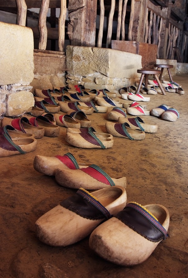 Mehrere Paar Holzschuhe stehen auf Stampflehmboden.