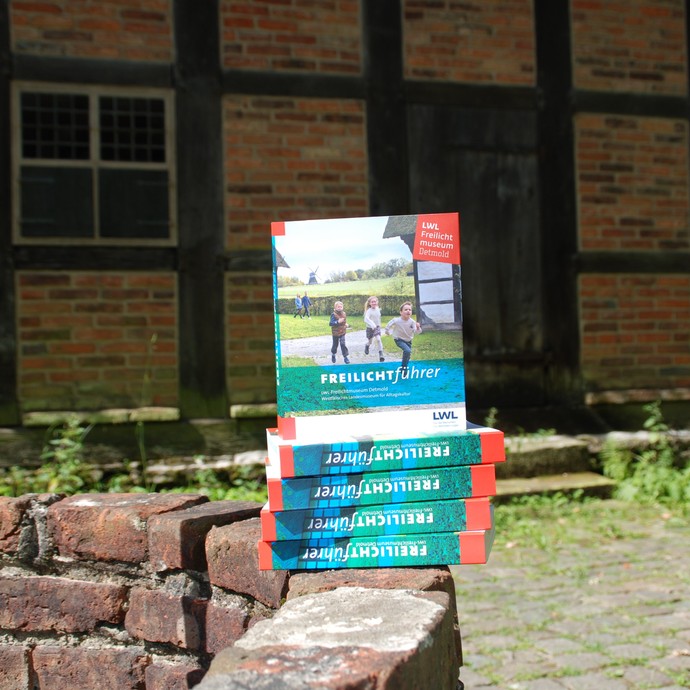 Ein Stapel Museumsführer liegt auf einer Backsteinmauer, im Hintergrund ein Fachwerkgebäude. (vergrößerte Bildansicht wird geöffnet)