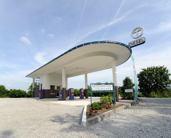 Eine Tankstelle aus den 1960er Jahren mit einem halbrunden Dach, darunter zwei Zapfsäulen.