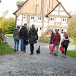 Eine Gruppe Erwachsener vor einem Fachwerkhaus, in der Mitte eine schwarze Ente.
