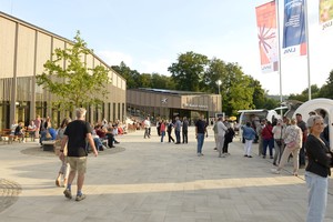 Auf einem großen Platz gehen viele Menschen. Dahinter steht das Museums-Gebäude.