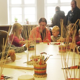 Im Vordergrund ist eine geflochtene Stiftedose zu sehen, die Teilnehmenden eines Workshops im Hintergrund.