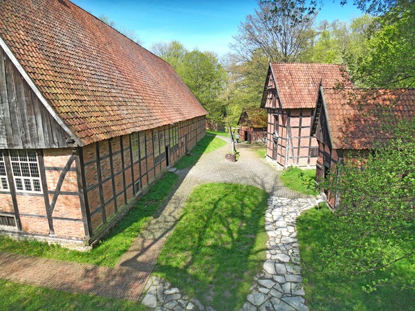 Links ein großes Fachwerkhaus, rechts drei kleinere Fachwerkhäuser, dazwischen ein geschotterter Weg.